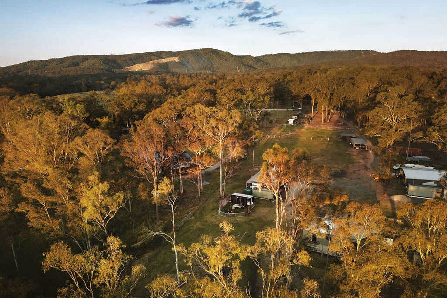 Une propriété rurale comprenant plusieurs bâtiments, entourée d’une forêt dense et de collines.