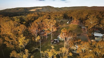 Une propriété rurale comprenant plusieurs bâtiments, entourée d’une forêt dense et de collines.