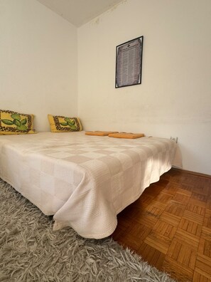 A bedroom with a bed, two pillows, a wall-mounted picture, and a wooden floor. - Lorik Studio Apartment (Prishtinë)