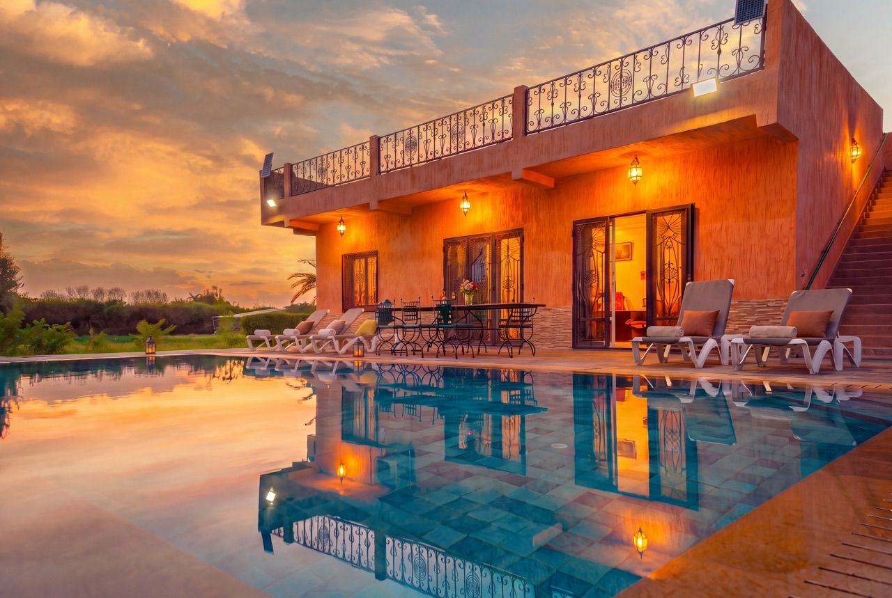 A modern two-story building with a swimming pool, outdoor seating, and a balcony with decorative railing.