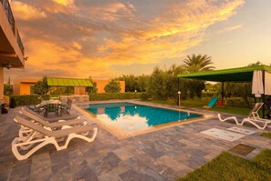 Una piscina con sillas de descanso, una mesa y un tobogán, rodeada de vegetación y edificios.