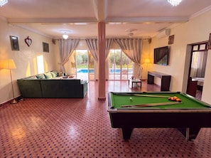 Sala de juegos con mesa de billar, un sofá y vista a una piscina.