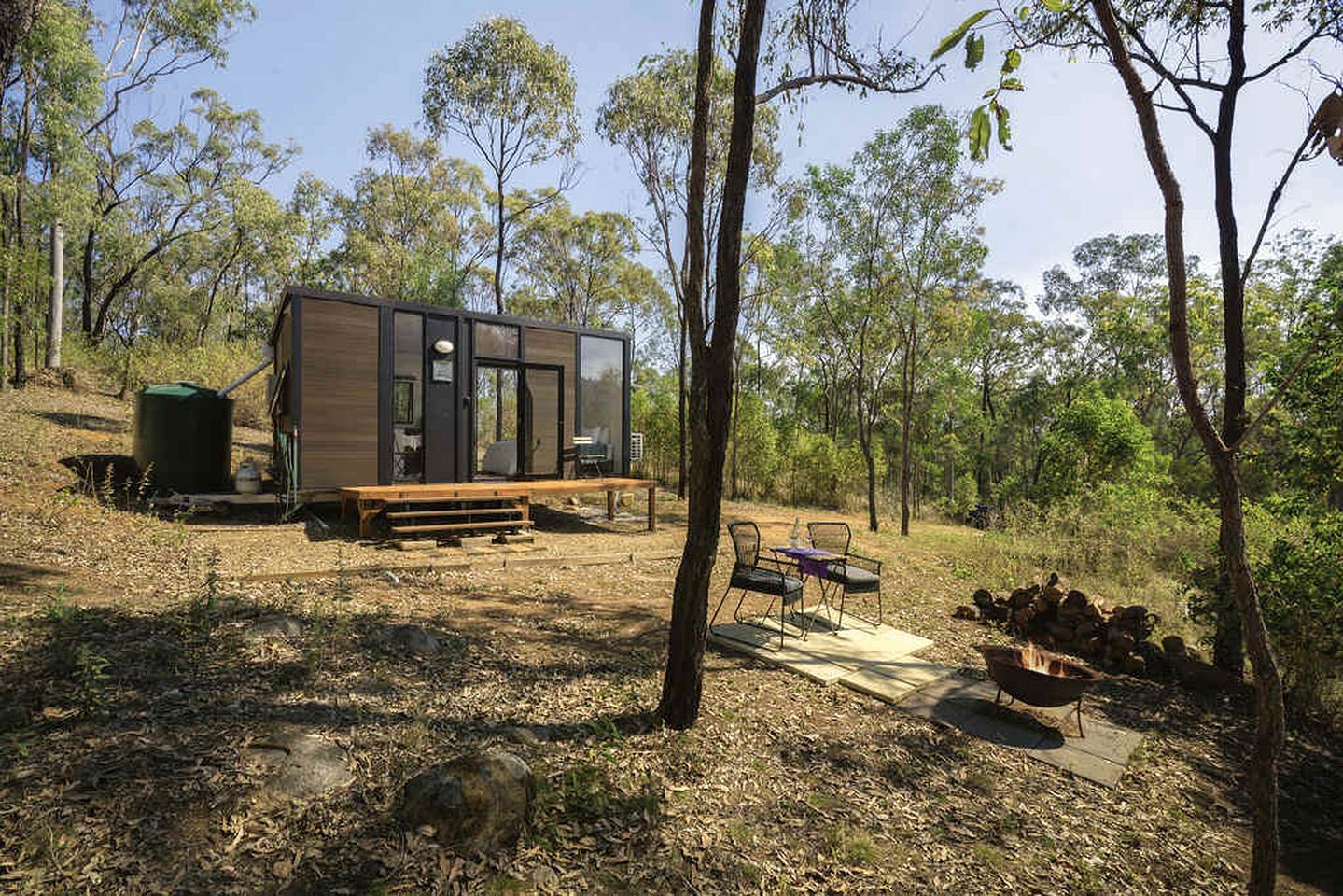 A modern cabin with a deck, surrounded by trees.