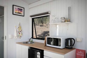 A compact kitchen with a microwave, kettle, and a window overlooking a forest.