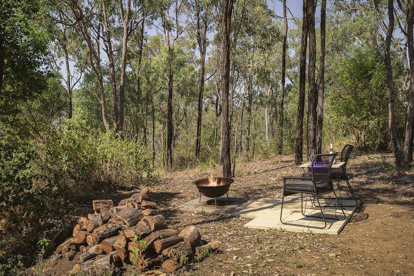 Un camping con una fogata, una mesa y sillas de metal, y una pila de leña.