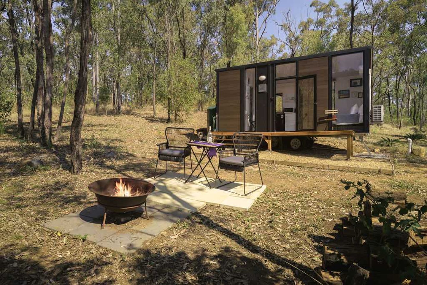 A modern cabin with a fire pit and outdoor seating, surrounded by trees.