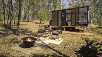 A modern cabin with a fire pit and outdoor seating, surrounded by trees.