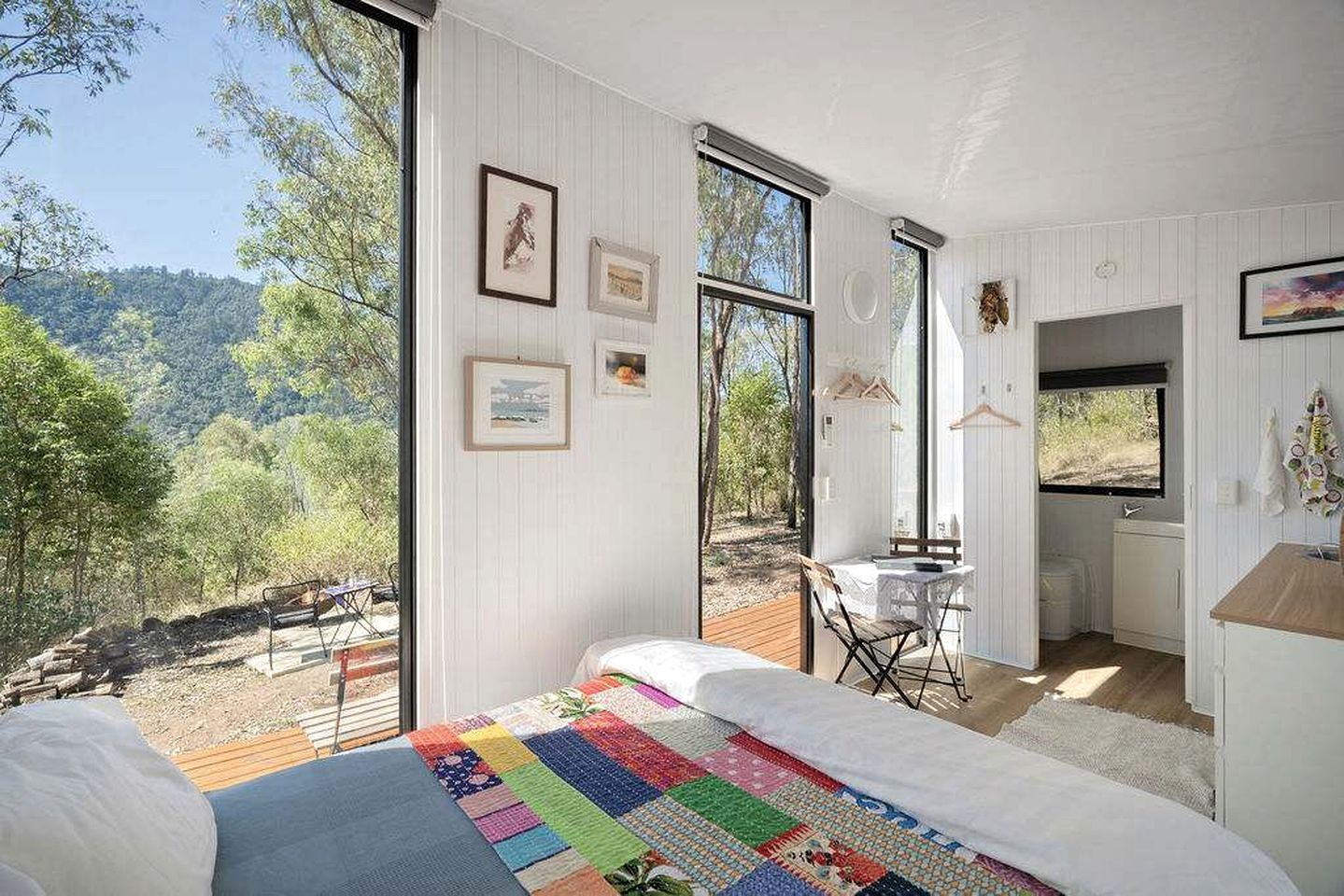 A bedroom with a large bed, a view of the outdoors, and a small table with a chair.