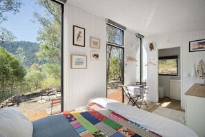 A bedroom with a large bed, a view of the outdoors, and a small table with a chair.