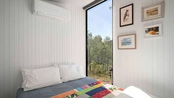 Un dormitorio con una cama, un colcha colorida, una ventana con vista a árboles y cuadros en la pared.