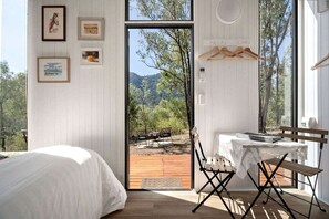 A bedroom with a bed, a table with chairs, and a view of the outdoors through a door.