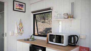 A compact kitchen with a microwave, kettle, and a window overlooking a forest.