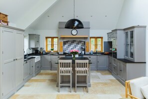 A modern kitchen with grey cabinetry, a central island with two chairs, a black pendant light, and a clock on the wall. - The Old Stables - Country Retreat (Swindon)