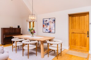 A dining area with a wooden table, six chairs, a vase with flowers, a painting on the wall, and a wooden door. - The Old Stables - Country Retreat (Swindon)