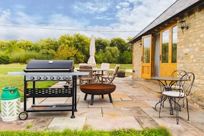 An outdoor patio with a barbecue grill, outdoor furniture, and a stone building with a yellow door. - The Old Stables - Country Retreat (Swindon)