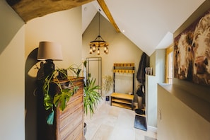 A hallway with a wooden dresser, a lamp, and a plant. There is a mirror on the wall and a bench with a coat rack. - The Old Stables - Country Retreat (Swindon)