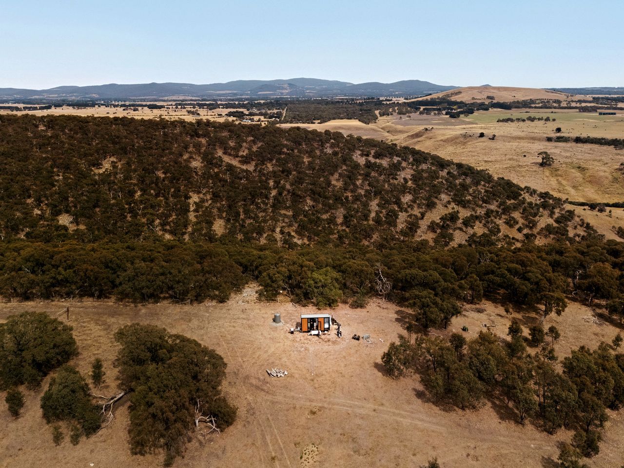 A remote, single-story building surrounded by dense forest and open fields.
