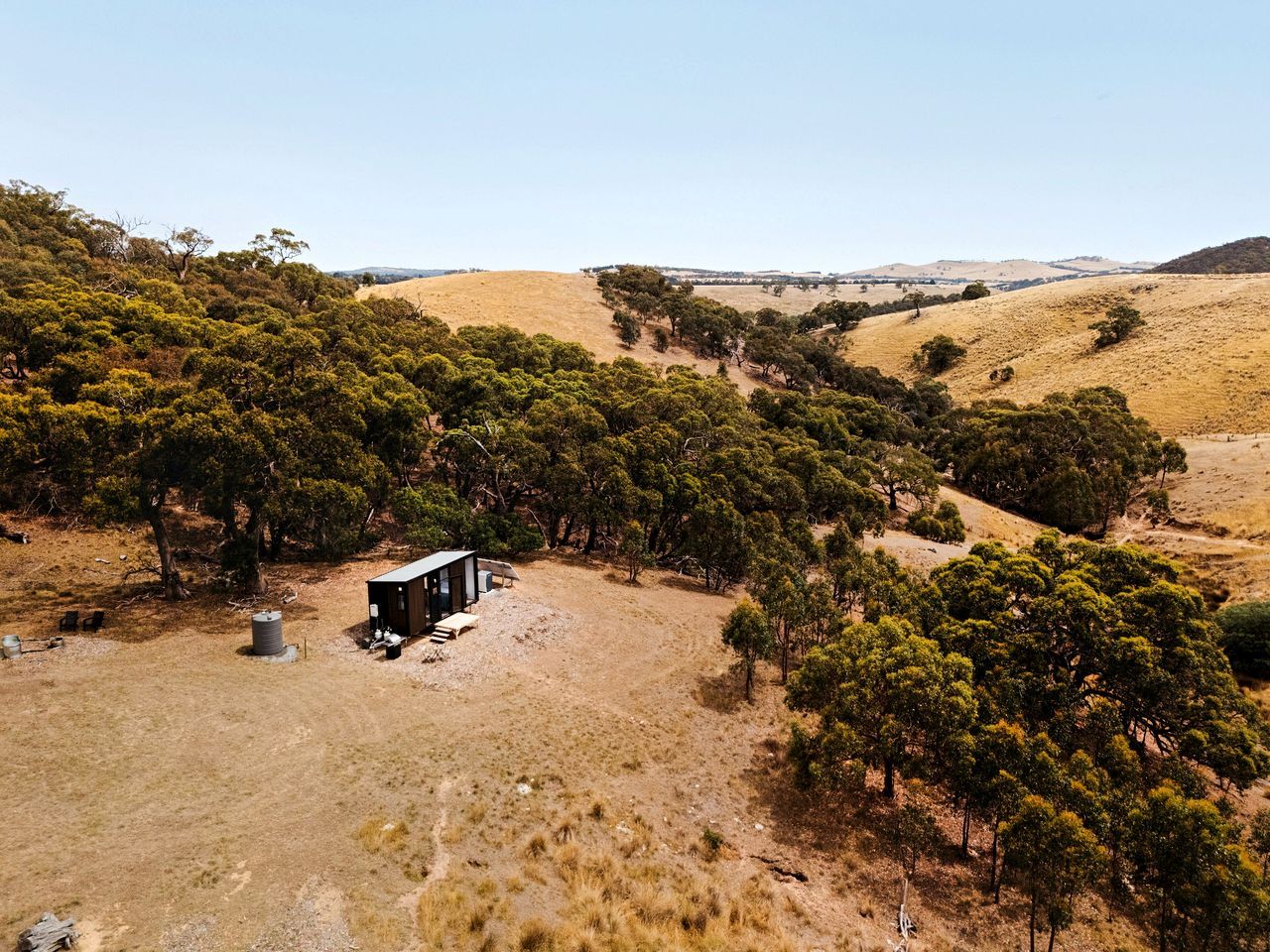 A remote cabin surrounded by dense trees and dry grassland.