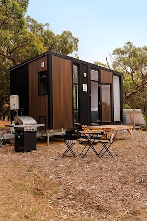 Een compact, modern vakantiehuisje met een ingebouwde grill en een tafel voor buiten eten.