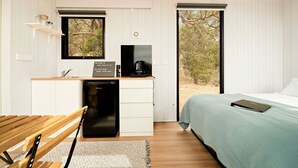 A compact room with a bed, a desk with a coffee maker, a small sink, and a window with a view of trees. - Magical Tiny House with Fantastic Vistas in Monegeetta, Victoria (Monegeetta)