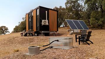 A modern, compact building with a black and wooden exterior, solar panels, and a firewood storage unit.
