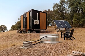 A modern, compact building with a black and wooden exterior, solar panels, and a firewood storage unit.