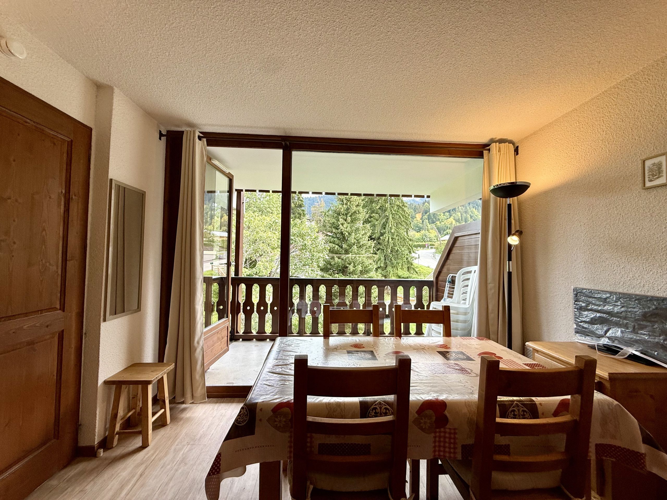 A dining area with a table and chairs, a bench, a view of greenery through a sliding door, and a lamp.