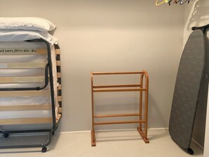 Uma cama beliche com colchão, uma estante de madeira e um centro de passar roupa fixado na parede.