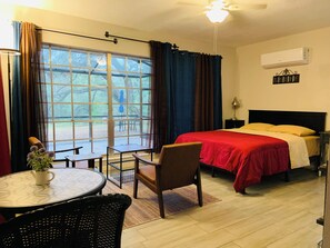 Ein Hotelzimmer mit einem Bett, einem Tisch mit Stühlen, einem Fenster mit Vorhängen und einer Klimaanlage.