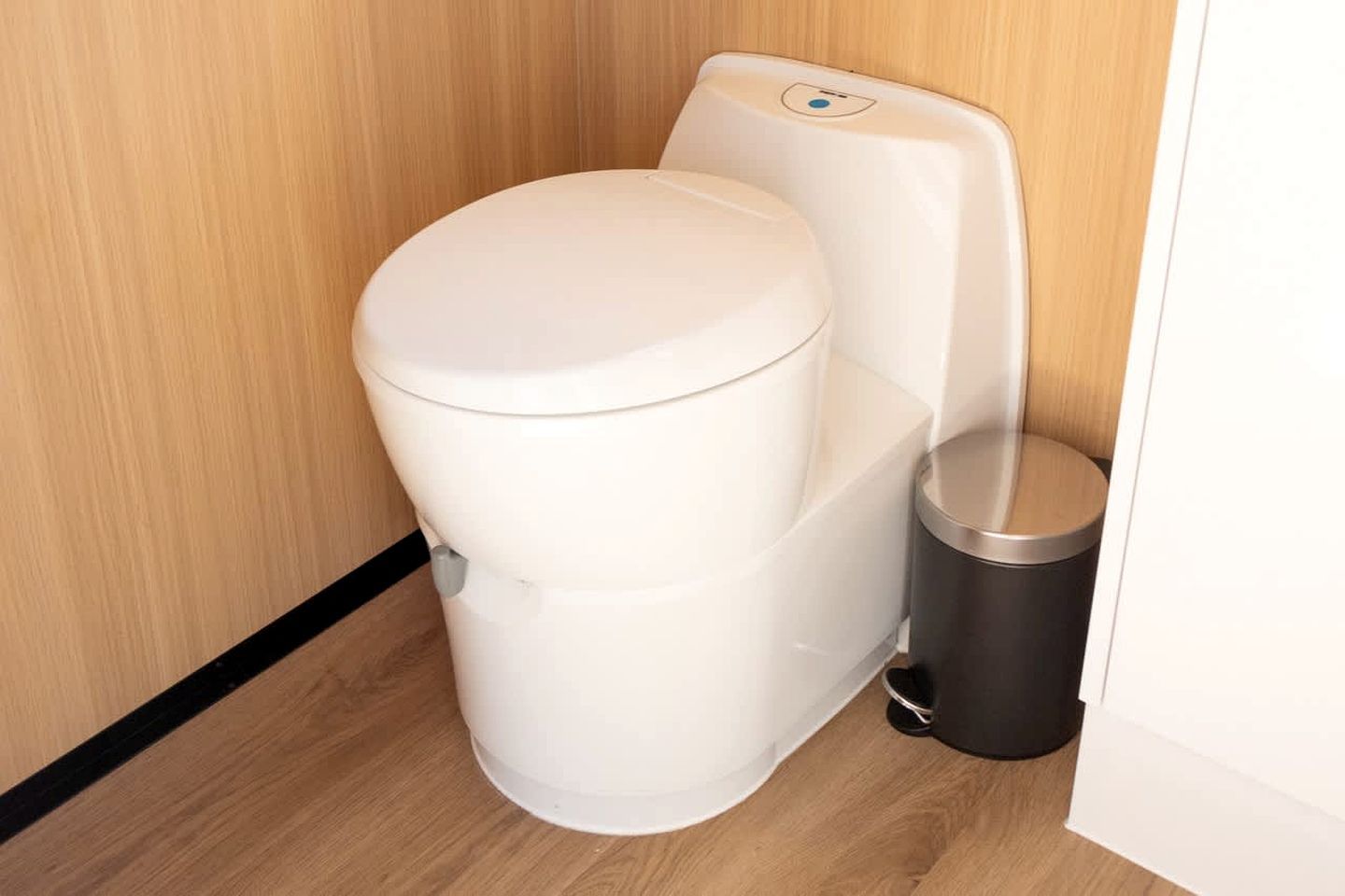 A white toilet with a flush handle and a trash bin beside it.