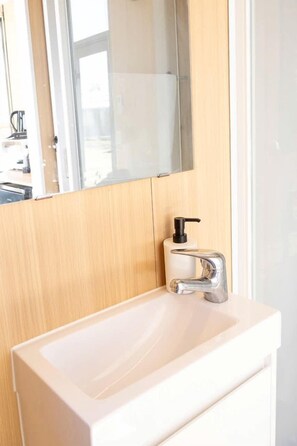Une salle de bain avec un lavabo blanc, un distributeur de savon noir et un miroir au-dessus du lavabo.