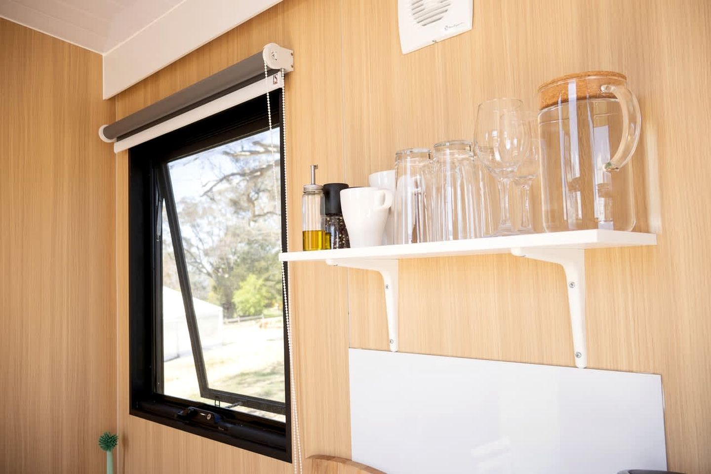 A window with a black frame, a white shelf with glassware, and a whiteboard below.