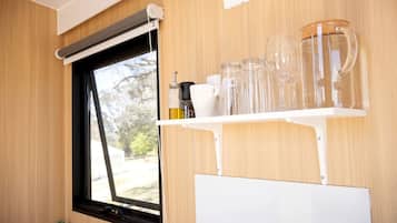 A window with a black frame, a white shelf with glassware, and a whiteboard below.