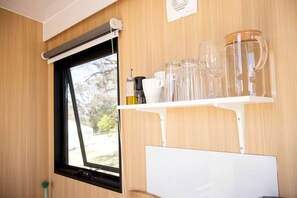 A window with a black frame, a white shelf with glassware, and a whiteboard below.