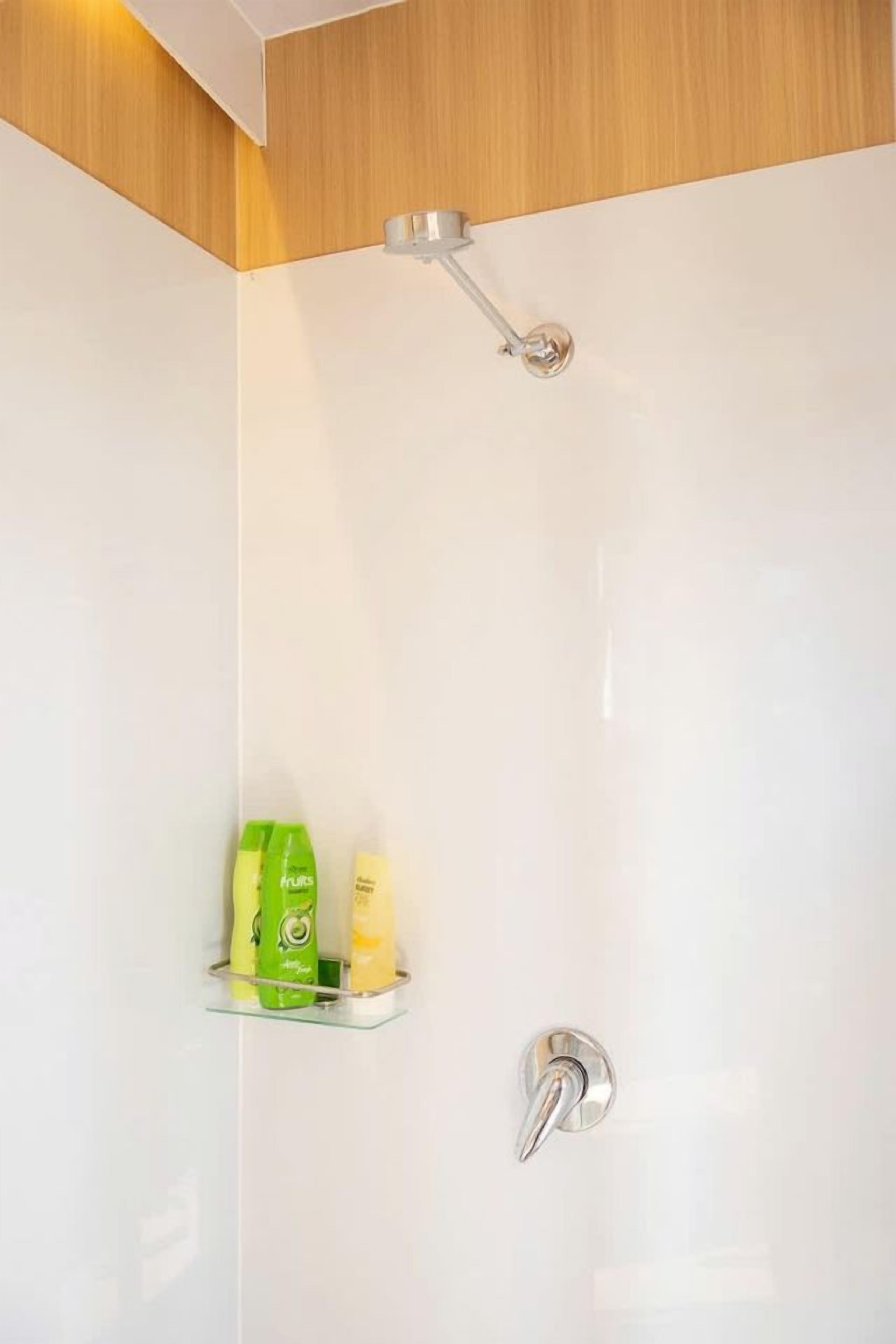A shower with a handheld showerhead and a wall-mounted faucet. There is a shelf with toiletries.