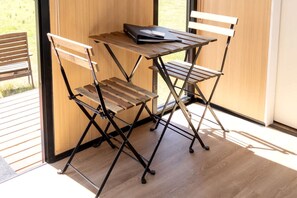 Une petite table en bois, sur laquelle repose un dossier noir, est flanquée de deux chaises en bois à ossature métallique.