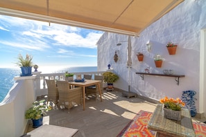A balcony with wicker furniture, potted plants, and a view of the sea. - Apartment in Nerja Near Playazo Beach (Nerja)
