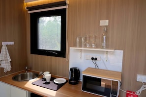 Cocina compacta con ventana, un lavamanos, microondas y una estantería con cristalería.