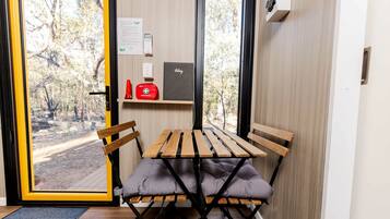 Une pièce avec une table et des chaises, une porte donnant sur l’extérieur et une petite étagère contenant une trousse de premiers secours et un objet rouge.