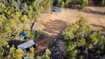 An aerial view of a property with a small cabin, a solar panel, and a dirt path surrounded by trees.