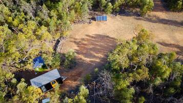 Vista aérea de uma propriedade com uma cabana pequena, um painel solar e uma trilha de terra cercada por árvores.