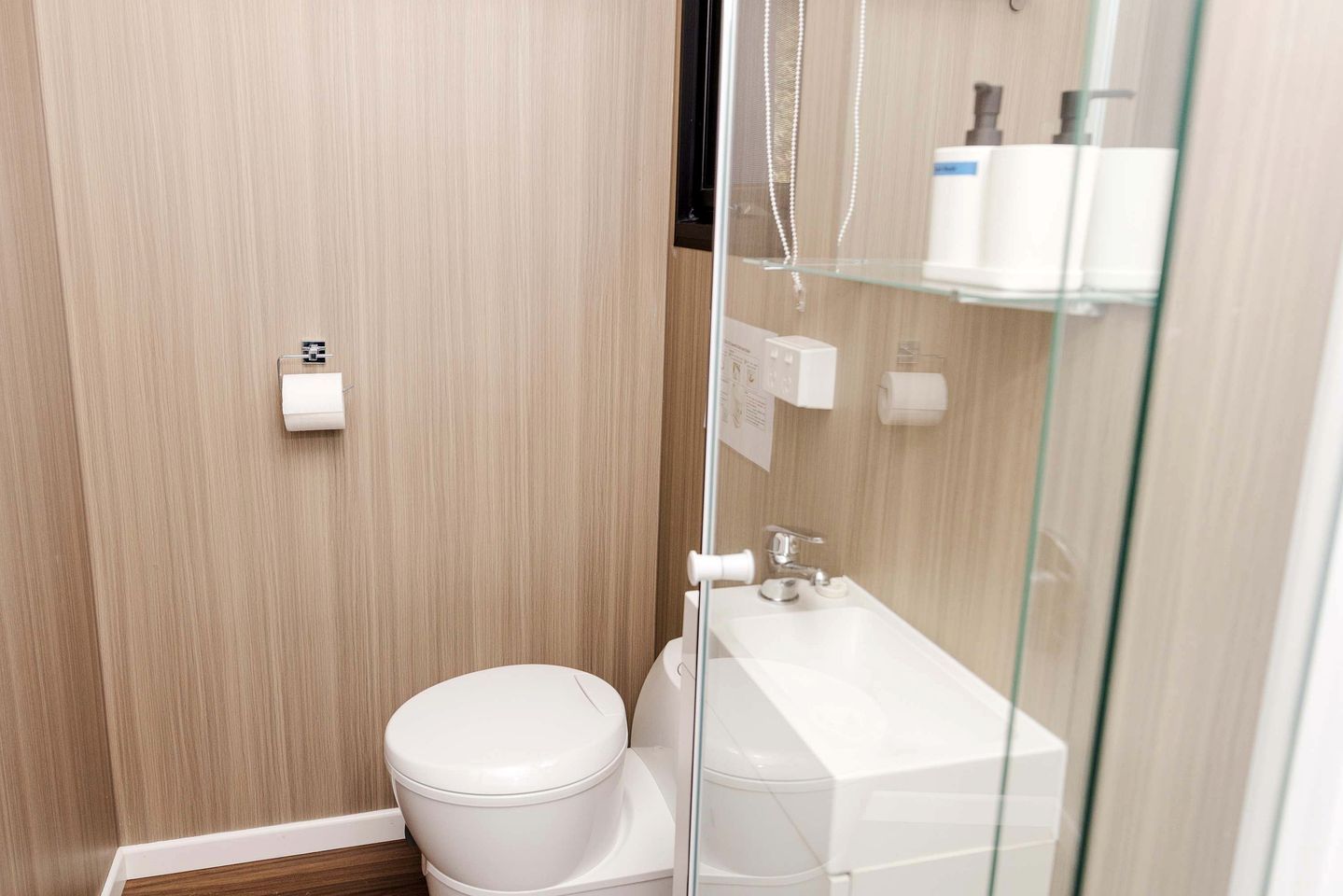 A modern bathroom with a toilet, a glass shower enclosure, and a white sink.