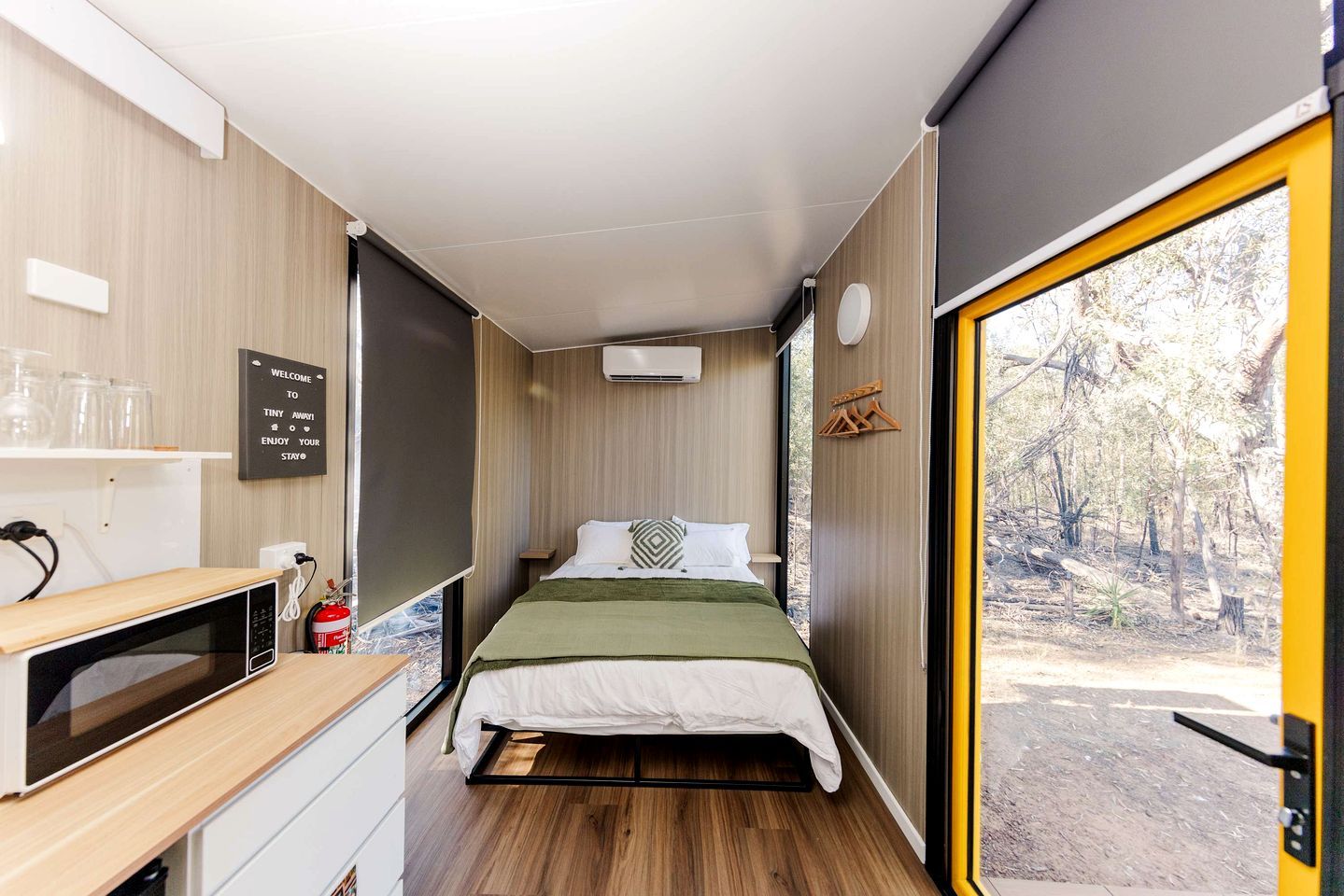 Une chambre de taille modeste, comprenant un lit, un four à micro-ondes, une petite table et une fenêtre donnant sur des arbres.