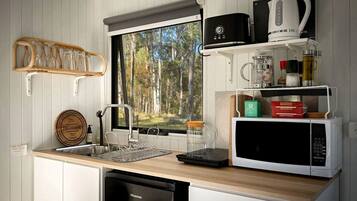 Cocina compacta con lavamanos, escurreplatos, microondas y ventana con vista a un bosque.