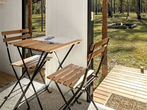 Un área de estar al aire libre con mesa y sillas de madera, un pozo de fuego y vistas al bosque.