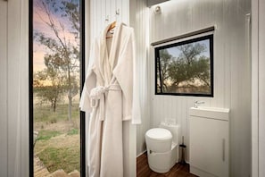 A bathroom with a window, a white toilet, a sink, and a robe hanging on a rack.