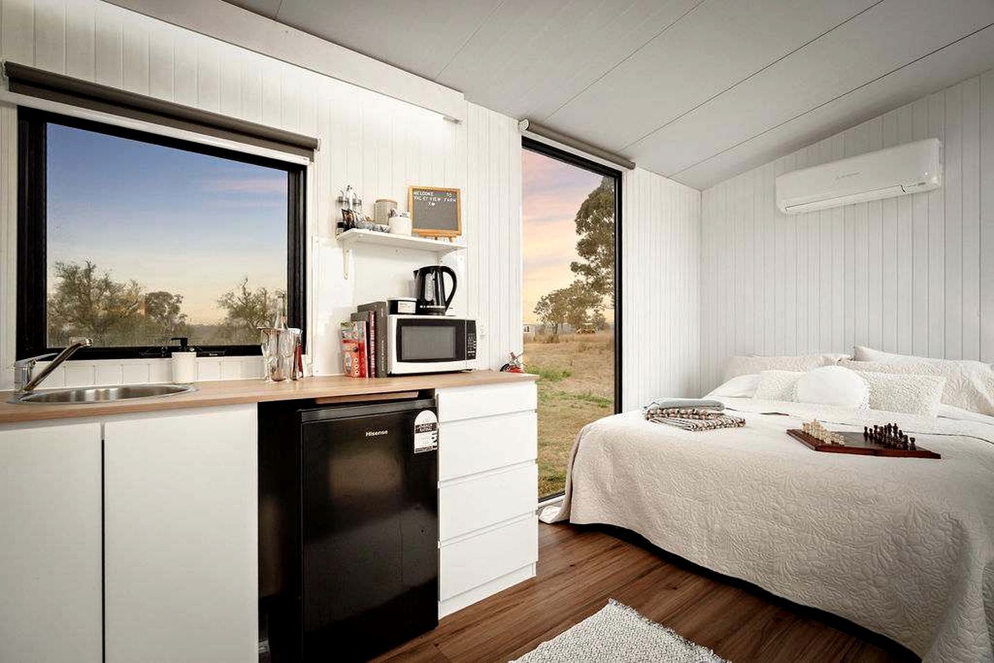 A compact bedroom with a bed, a small kitchenette, and a view of the outdoors.