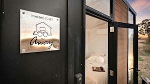 A sign indicating the property is managed by Away, with a view of a bedroom through a glass door. - Charming Tiny House with Panoramic Views of the Valley in Queensland, Australia (Goombungee)