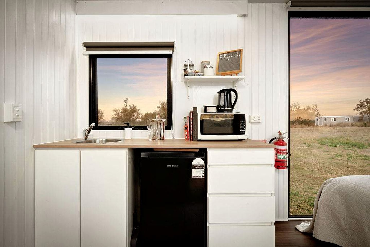 A compact kitchenette with a window, a microwave, a coffee maker, and a small shelf with items.