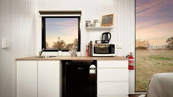 A compact kitchenette with a window, a microwave, a coffee maker, and a small shelf with items.